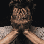 Man with disheveled hair covering face, expressing distress or confusion.