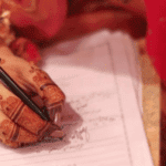 Bride's hand with henna designs signing marriage document at nikah.